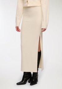 Gonna midi a costine color crema con spacco laterale indossata con stivali alti neri con tacco e un maglione abbinato color crema.