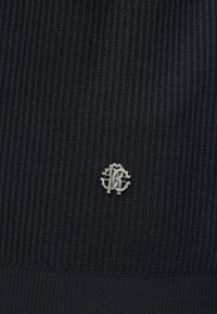 Tissu côtelé noir avec un petit emblème monogramme argenté présentant les lettres "B" et "C" entrelacées au centre.