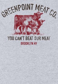 Maglietta grigia con una grafica di due mucche e testo rosso e nero che recita "Greenpoint Meat Co." e "Non puoi battere la nostra carne, Brooklyn, NY."