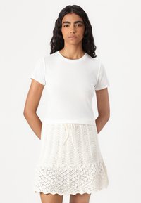 Top blanco de manga corta combinado con una falda de encaje texturizado en color crema, con cintura ajustable y dobladillo con picos.