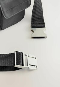 Borsa nera in nylon con finitura testurizzata, dotata di una fibbia e di una tracolla in metallo argento, posizionata su uno sfondo chiaro.