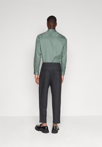 Grön långärmad skjorta med knappar och en bakfåll, kombinerad med mörkgrå skräddarsydda byxor med dragsko i midjan och bakfickor.