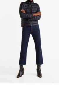 Czarna pikowana kurtka z wysokim kołnierzem, zamek z przodu; połączona z ciemnoniebieskimi, krótkimi dżinsami i czarnymi botkami na obcasie z ostrymi noskami.