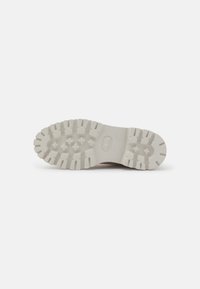 Semelle en caoutchouc blanc avec un motif texturé, avec de profonds cannelures et un logo central. Surface lisse avec un design plat et robuste.