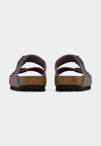 Ζευγάρι μοβ σουέντ σανδάλια με διπλούς ρυθμιζόμενους ιμάντες και υφασμένα καφέ φελλό πέλματα, εμφανιζόμενα από πίσω σε λευκό φόντο.