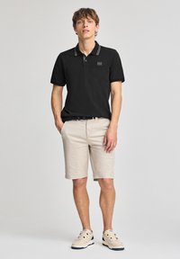 Svart polotröja med randig krage, i kombination med beige shorts. Avslappnade skor kompletterar outfiten, med en strukturdesign.