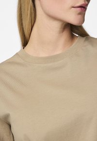 Μπεζ βαμβακερό t-shirt με στρογγυλή λαιμόκοψη και κοντά μανίκια, με λεία υφή και διακριτή ραφή κατά μήκος του γιακα.