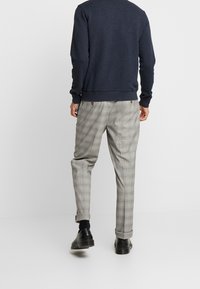 Maglione blu navy con orlo a coste, abbinato a pantaloni a quadri grigio chiaro con risvolti e calzature scure.