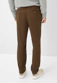 Chinos marron avec une texture lisse, dotés de poches arrière à boutons, associés à des baskets beiges. La ceinture ajustable est visible.
