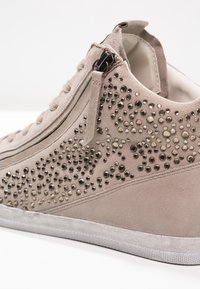 Beige mockask högtoppssneaker med dekorativa metallnitar, sidodragkedja och strukturerad gummisula. Slät foder och vadderad krage.