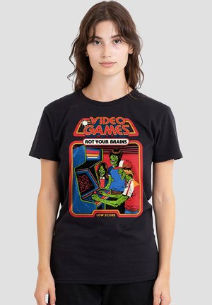 Young woman wearing black t-shirt with colorful graphic of three green zombies playing an arcade video game labeled “Video Games Rot Your Brains Low Score.”