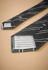 Schleife in Schwarz mit einem diagonal gestreiften Muster in Grau. Strukturierter Stoff mit einem scharfen Schnitt und kontrastierendem gestreiften Futter.