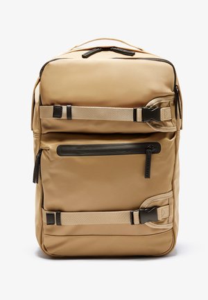 Beige rugzak met twee horizontale verstelbare riemen en gespen, een ritsvak aan de voorkant en een draaghendel bovenaan.