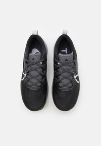 Baskets de sport noires avec une tige en maille, des accents gris et un logo blanc. Présentent une surface texturée et un laçage élastique pour un ajustement sécurisé.