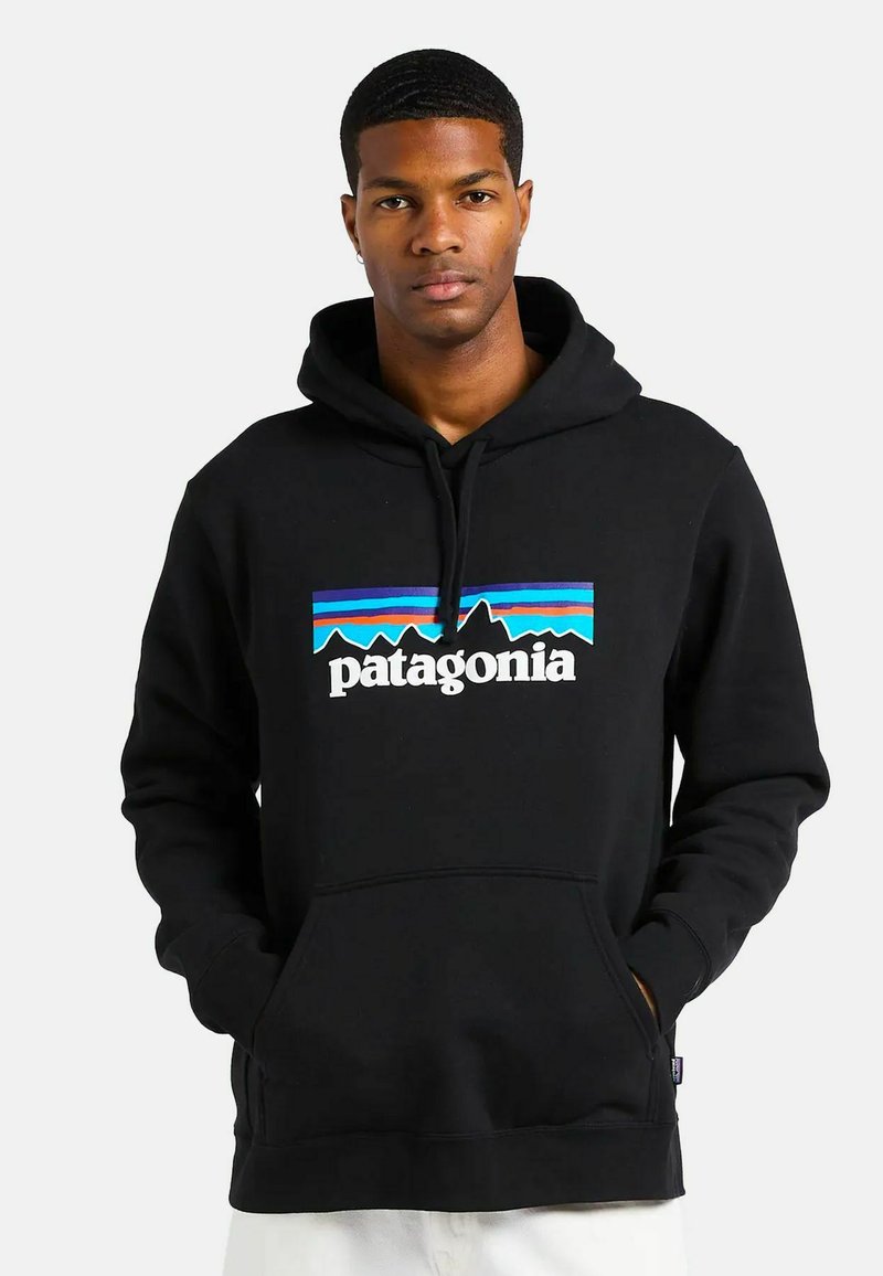 Schwarzer Hoodie mit Kängurutasche, der ein farbenfrohes Bergmotiv und den Text "patagonia" auf der Vorderseite zeigt. Weicher, strukturierter Stoff.