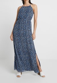Maxiklänning i marinblått med ett blått och vitt blommönster, halterneck och sidospalt. Tillverkad av lätt tyg, med en avslappnad passform.