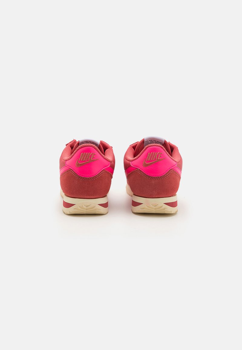 Baskets Nike rouges et roses avec un supérieur en daim et en mesh, un col rembourré et une semelle en caoutchouc texturé avec un logo visible sur le talon.