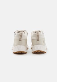 Baskets de sport blanches avec une surface texturée, tige en mesh et semelle extérieure en caoutchouc. Les caractéristiques incluent des languettes de traction et des détails de marque sur le talon.