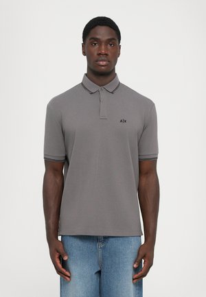 Man wearing gray short-sleeve polo shirt with black trim and A|X logo, paired with light blue jeans, standing against a plain background.
