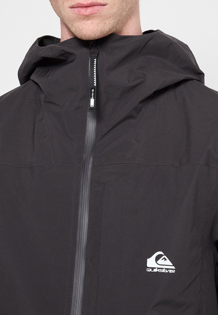Chaqueta impermeable negra con cremallera frontal y capucha. Presenta una textura sutil y el logo de Quiksilver en el lado izquierdo del pecho.