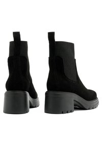 Black suede ankle boots with ribbed fabric accents, chunky heel, and pull tabs at the back. Textured rubber sole for traction.