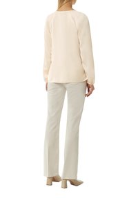Hellbeige Bluse mit langen Ärmeln, glatter Textur, Rundhalsausschnitt und elastischen Bündchen. Kombiniert mit cremefarbenen Schlaghosen und nudefarbenen Blockabsätzen.