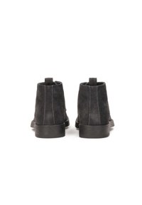 Botas de tobillo de ante negro con un tacón de goma bajo, que presentan costuras en contraste y tiradores en la parte posterior para facilitar su uso.