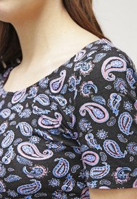 Top negro de manga corta con un colorido estampado de paisley en rosa y azul. La tela parece suave con una textura lisa.