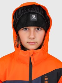 Bambino con giacca arancione con cappuccio e berretto di maglia nera con logo "Brunotti", che guarda dritto davanti a sé su uno sfondo neutro.