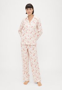 Conjunto de pijama floral em tecido suave; camisa de botão de manga longa com gola em ponta, calças correspondentes com cintura elástica, padrão em rosa claro e verde.