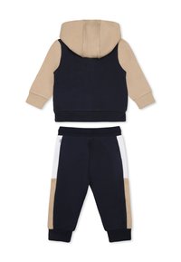 Ensemble de sweat à capuche et de pantalon en bleu marine et beige. Tissu doux, design color-block, avec des rayures blanches et beiges sur le pantalon. Poignets et taille élastiques.