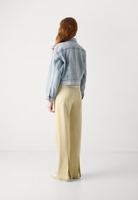 Lichte denim cropped jack, beige wijde broek met zijsplitten, en witte sneakers. De setting is minimalistisch met een effen achtergrond.