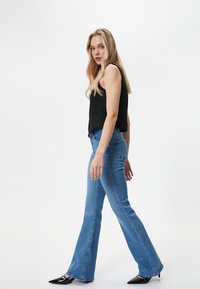 Top negro sin mangas, jeans acampanados azules y tacones negros de punta. Tela suave, corte ajustado, con detalles de costura frontal en los jeans.