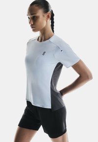 T-shirt de sport bleu clair avec des panneaux latéraux noirs, manches courtes et encolure arrondie. Dispose d'un logo sur la poitrine et d'un design épuré.