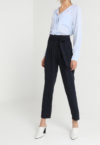 Ljusblå blus med lång ärm och V-ringning. Mörkblå randiga byxor med slipsbälte, slim fit. Vita klackskor fulländar outfitten.