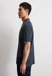 Dark navy polo shirt with contrasting light blue collar and sleeve trim, made from textured cotton fabric, featuring a relaxed fit design.