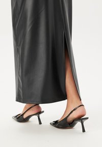 Zwarte leren maxi-rok met een zijsplit. G gedragen met zwarte slingback hakken met strikdetail en een spitse neus.