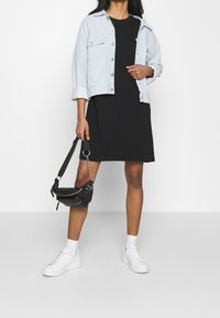 Ljusblå denimjacka, svart knälång klänning, svart handväska, vita sneakers och vita strumpor. Jackan har knappar och uppvikta ärmar.