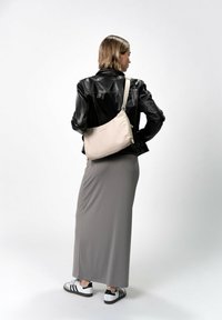 Borsa a spalla beige realizzata in un materiale morbido, con una forma curvata, chiusura zip e tracolla regolabile. Indossata con una gonna grigia e una giacca nera.