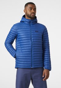 Chaqueta de plumas azul con diseño acolchado horizontal, cierre frontal con cremallera y capucha. Presenta un pequeño logo en el lado izquierdo del pecho y puños elásticos.