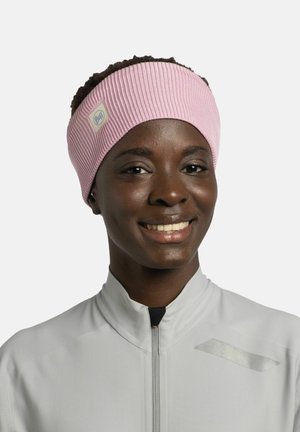 Rosa gerippte Haarband mit einem Stoffetikett, getragen von einer Person in einer hellgrauen Zip-Jacke, hat eine insgesamt glatte Textur.