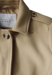 Beige villa sekoitettu takki, jossa on lovettu kaulus, kaksi marmorikuvioista nappia ja "Street One Studio" -etiketti.