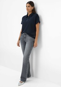 Polo shirt navy con colletto e placket a tre bottoni, abbinato a jeans svasati grigi e scarpe argento con punta a punta. Tessuto liscio.