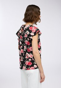 Blusa floreale con sfondo nero, maniche a balze e dettaglio a chiave sul retro. Presenta motivi di rose rosse e rosa su un tessuto leggero.