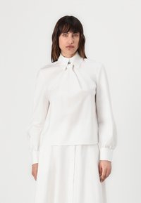 Hvit langermet bluse med strukturert krage, frontfolding og knappede mansjetter, laget av glatt stoff med en ren finish.