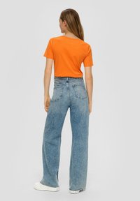 Oranje katoenen T-shirt gecombineerd met lichtblauwe wijde jeans. De jeans hebben een hoge taille en achterzakken, met een ruwezoomafwerking aan de mouwen.