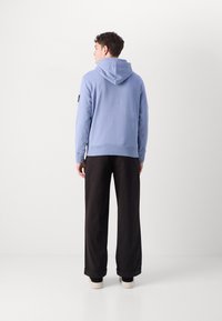 Hanorac bleu deschis cu glugă ajustabilă, manșete și tiv ribbrate. Asortat cu pantaloni negri cu picioare late și încălțăminte deschisă.