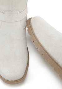 Stivaletti in suede bianco alla caviglia con suola in gomma piatta, punta rotonda e dettaglio con cinturino alla caviglia. Texture liscia e design minimalista.