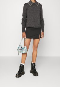 Szary sweter z kołnierzem zdobionym ćwiekami, czarna mini spódnica z bocznym rozcięciem oraz czarne botki na sznurowadła. Nosi małą, połyskującą torebkę.