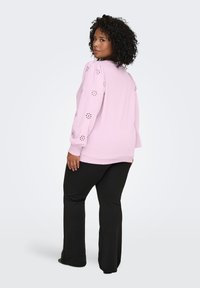 Light pink sweatshirt with puffed sleeves featuring cut-out floral designs. Black flared pants complete the outfit.